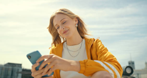 Woman in yellow jacket using smartphone outdoors, symbolizing mobile app development user experience.